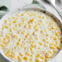 Creamy corn casserole in white bowl with black pepper topping, baked comfort food, easy corn casserole recipe, cheesy baked corn dish.