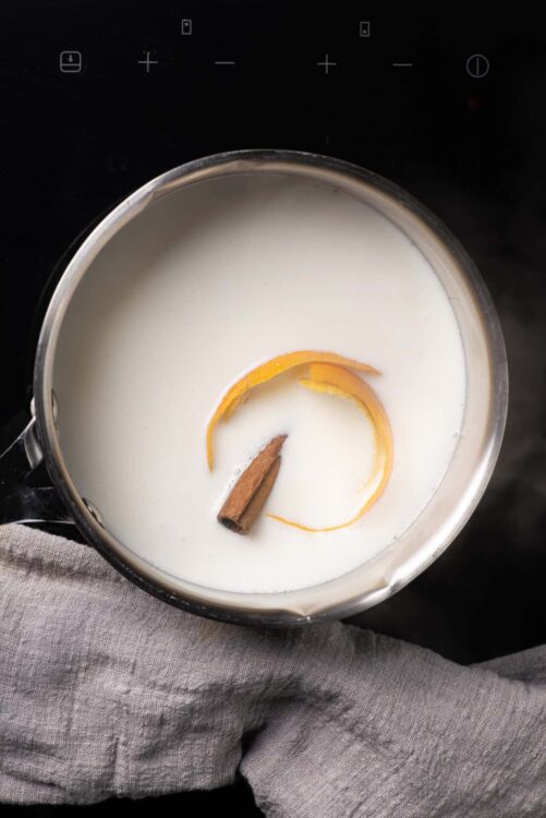 Creamy milk with orange peel and cinnamon stick, ready for cooking or brewing.