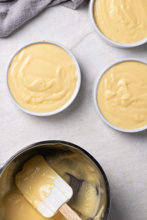 Smooth homemade vanilla custard in bowls with vanilla pudding in a mixing bowl.