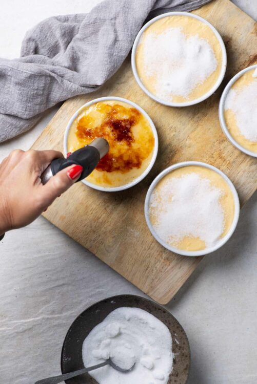 Creamy vanilla bean crème brûlée topped with caramelized sugar in small ramekins. Healthy breakfast or dessert with a crispy caramelized sugar top.