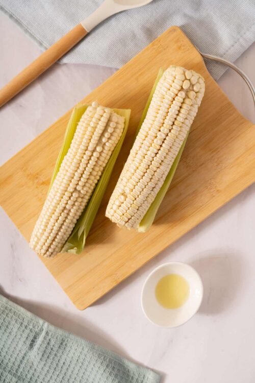 Fresh corn on the cob with husks partially removed, ready for boiling or grilling. Perfect summer favorite for cooking and recipes.