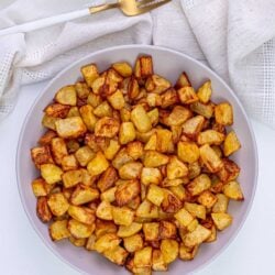 Crispy roasted potatoes on white platter with fresh parsley garnish.
