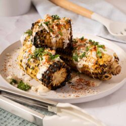 Grilled corn on the cob with creamy sauce, herbs, and spices served on a white plate.