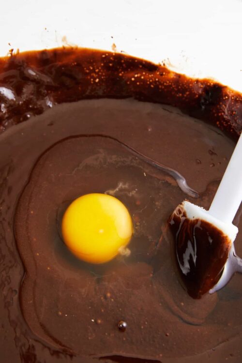 Creamy chocolate batter with a raw egg and spatula for baking preparation.