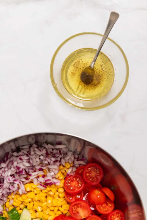 Golden olive oil with black pepper in a glass bowl with a spoon.