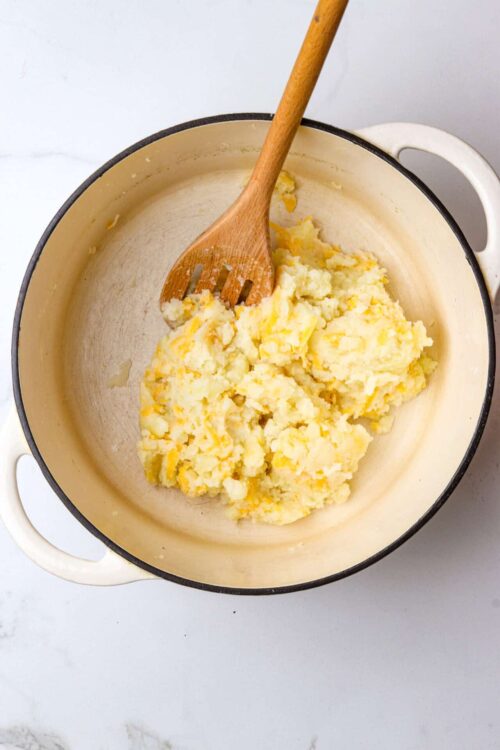 Creamed potatoes in a beige stove pot with a wooden spoon for baking recipes.