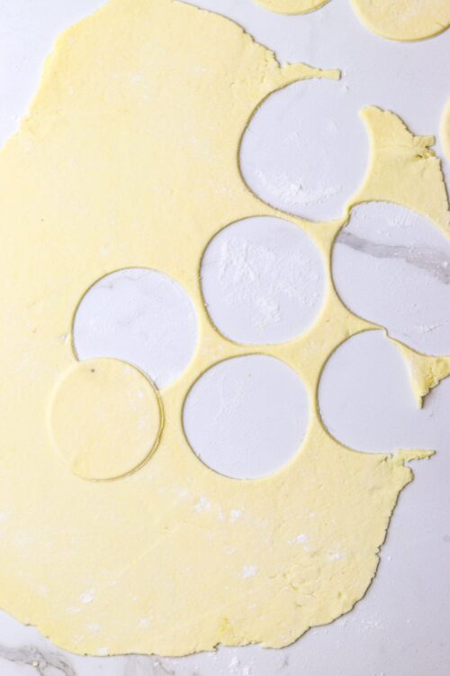Buttery pie dough rolled out with circular cookie cutter cutouts on a white marble surface.