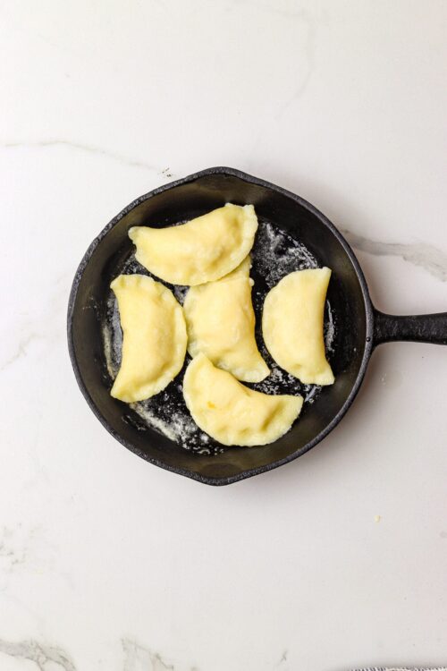 Golden fried pierogis in cast iron skillet on white marble surface.