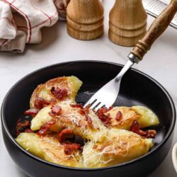 Golden baked stuffed peppers with bacon and cheese in a black bowl on a white surface with wooden salt and pepper shakers.