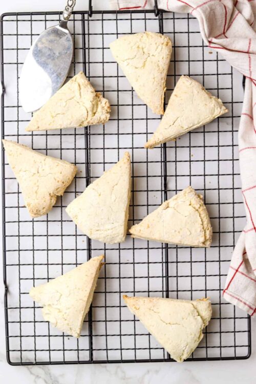 Fluffy scones cooling on a wire rack with a baking spatula and a red-striped kitchen towel.