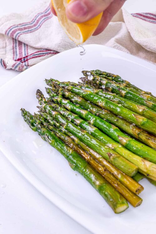 Roasted asparagus with lemon being drizzled with lemon juice at Baked Bree.