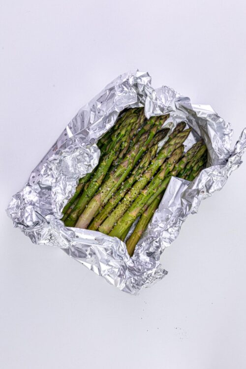 Fresh asparagus spears seasoned with salt and black pepper, ready for roasting in foil.