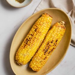 Grilled corn on the cob with charred kernels served on a beige platter.