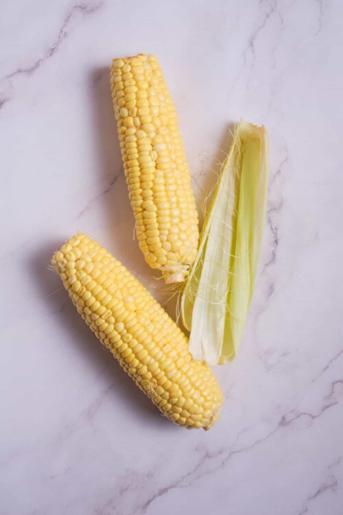 Fresh sweet corn on a white marble surface.