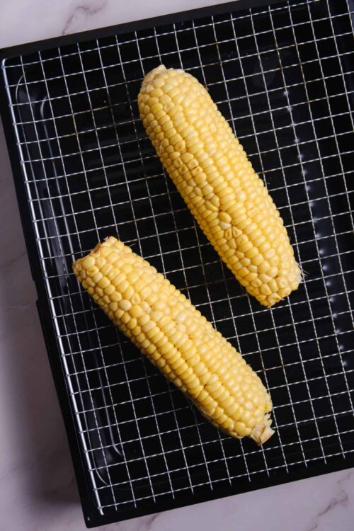 Sweet corn on a cooling rack for roasting or grilling. Fresh yellow corn cobs ready for cooking.