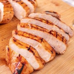 Juicy grilled chicken breast sliced on wooden cutting board.