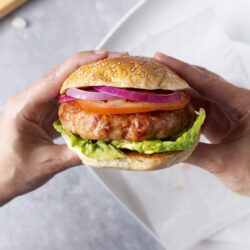 Juicy chicken burger with fresh vegetables and sesame bun on gray surface.