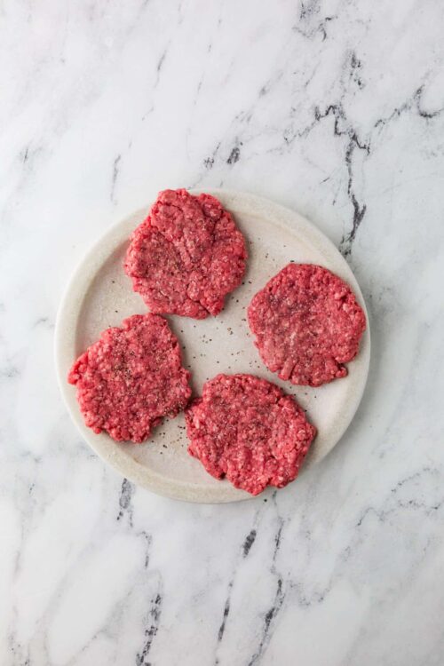 Fresh homemade raw beef patties on a round white ceramic plate.