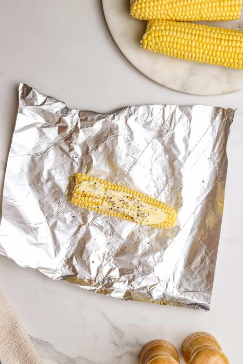 Fresh corn on the cob with seasoned butter on foil, ready to roast or grill.