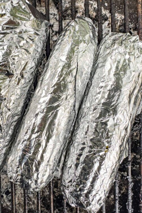 Foil-wrapped baked potatoes roasting on a barbecue grill for a delicious outdoor meal.