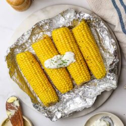 Golden grilled corn on the cob with butter and herbs on aluminum foil.
