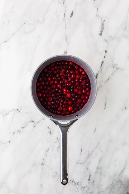 Fresh cranberries in a stainless steel colander on white marble countertop for baking recipes.