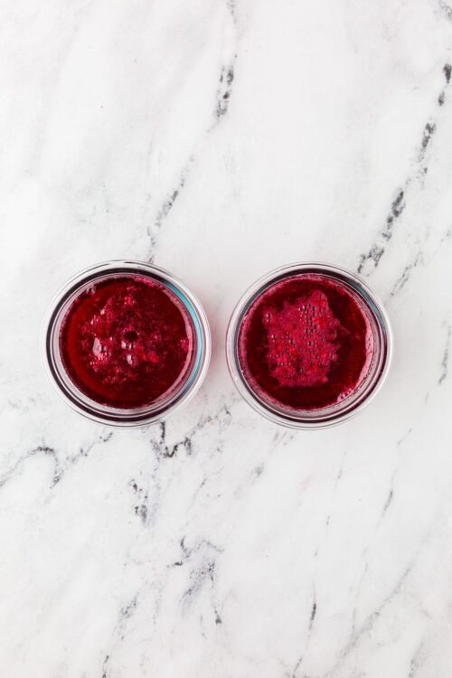 Bright red berry juice in two glasses on white marble surface.