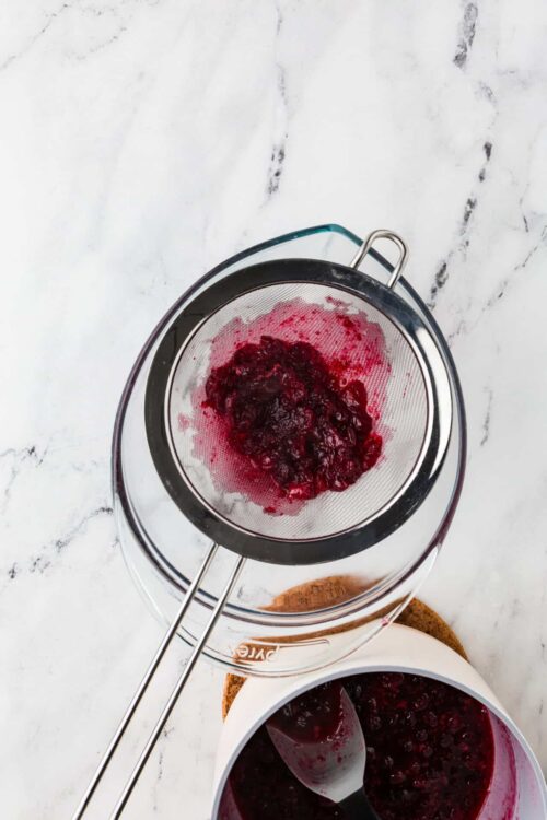 Fresh berry jam being strained with a fine mesh sieve.