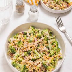 Fresh broccoli cauliflower chicken casserole in a white bowl with shredded cheese and bacon bits on top.
