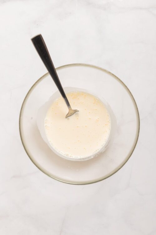 Cream mixture in clear glass bowl with silver spoon for baking recipe.