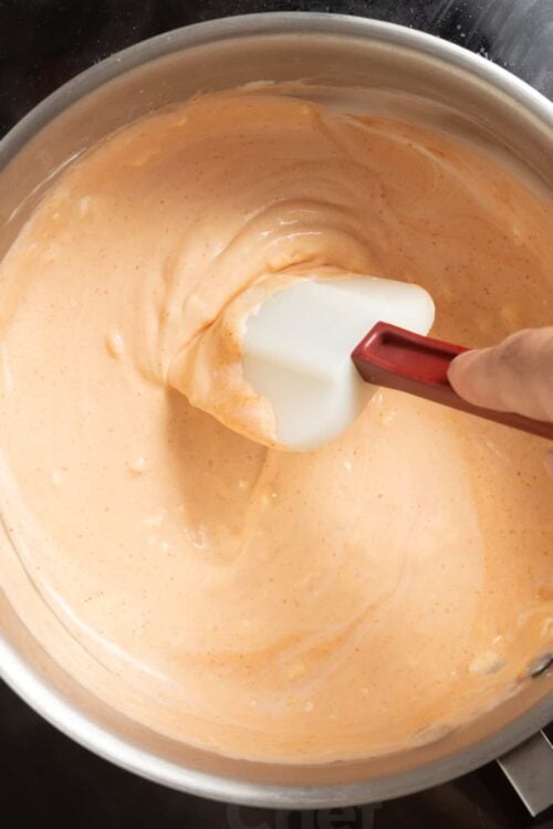 Creamy orange sauce being mixed in a stainless steel bowl with a spatula.