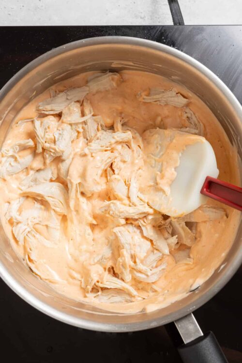 Creamy shredded chicken cooking in a skillet with orange sauce, ready for meal prep or sandwiches.