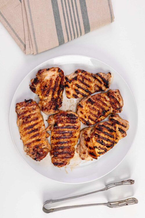 Grilled chicken breasts on a white plate with grill marks, served with a napkin and tongs.