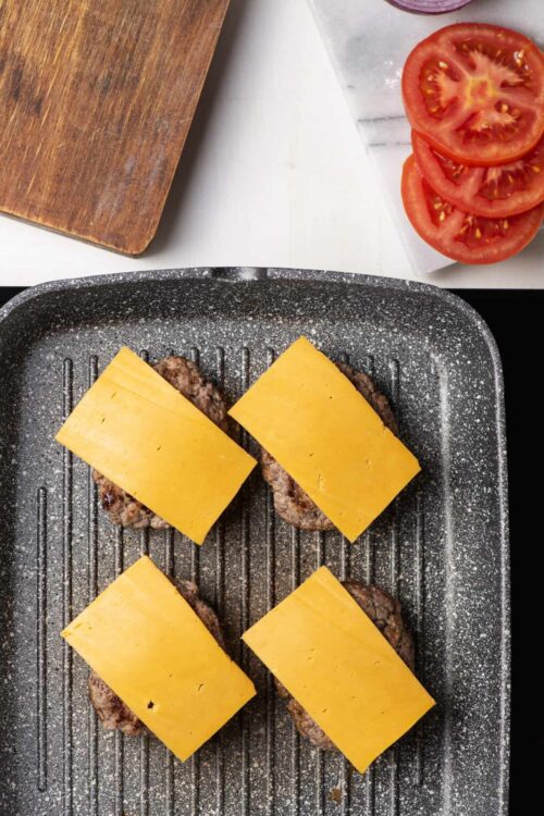Juicy cheeseburgers with melted cheddar on a black grill pan.