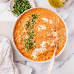 Creamy tomato soup with herbs and toppings on a white table, served as comfort food.
