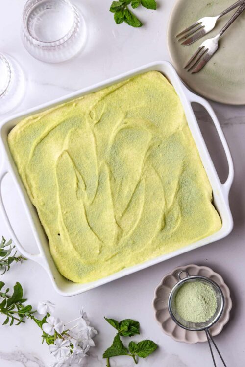 Fluffy lemon dessert in a white baking dish with mint and floral garnishes.