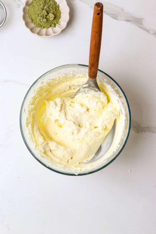 Fluffy homemade buttercream frosting in a glass bowl with a wooden spoon.