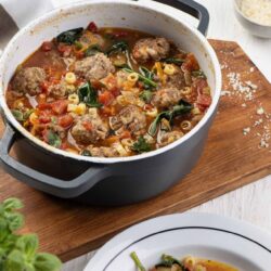 Savory meatball soup in a white skillet with chopped tomatoes and pasta, cozy comfort food.
