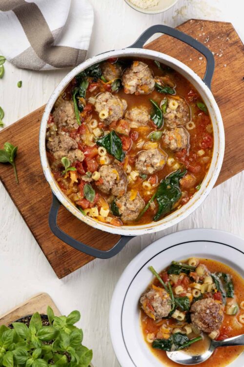 Savory homemade meatball stew with spinach and pasta in a white enamel pot, ready to serve.