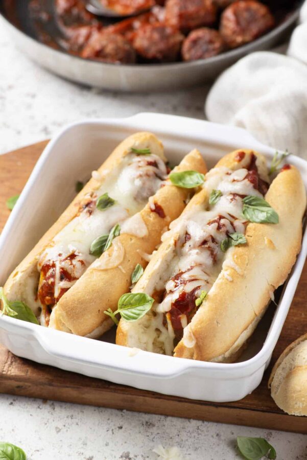 Soft Italian meatball subs with melted cheese and fresh basil in a white baking dish.