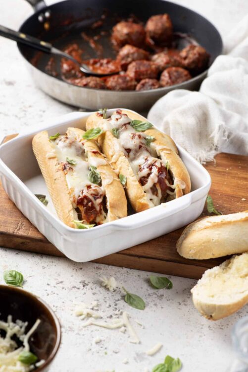 Savory Italian sausage and melted cheese sandwiches with fresh basil on a baking sheet.