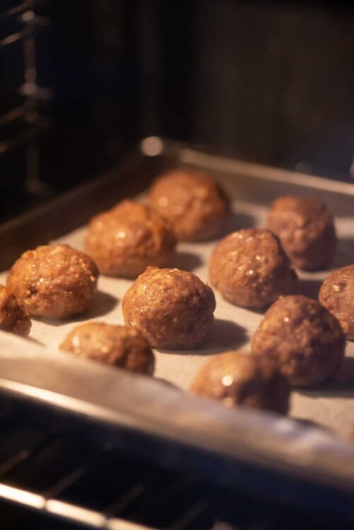 Meatballs cooking in the oven on a baking sheet with parchment paper.