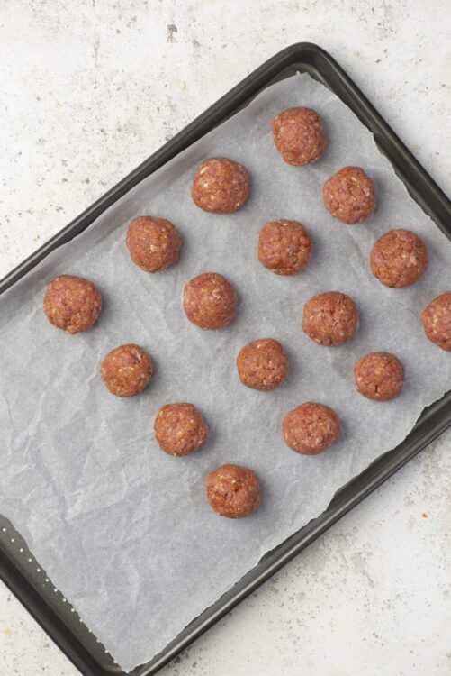 Crispy baked meatballs on baking sheet with parchment paper, homemade beef meatball recipe, easy baked meatballs, baked bree.