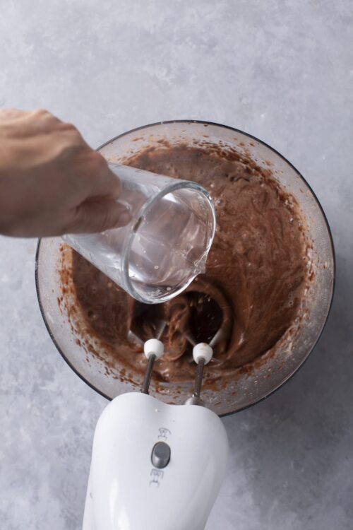 Silken chocolate cake batter being mixed in a stand mixer with water being added.
