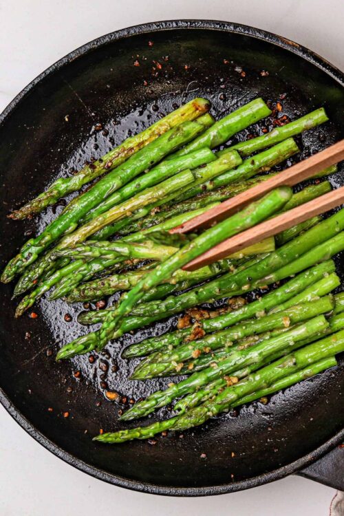 Sauteed asparagus in a black skillet with garlic and red pepper flakes, cooked to perfection.