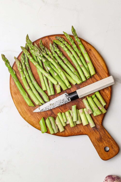 Freshly cut asparagus on a wooden cutting board with a knife, ready for cooking or roasting.