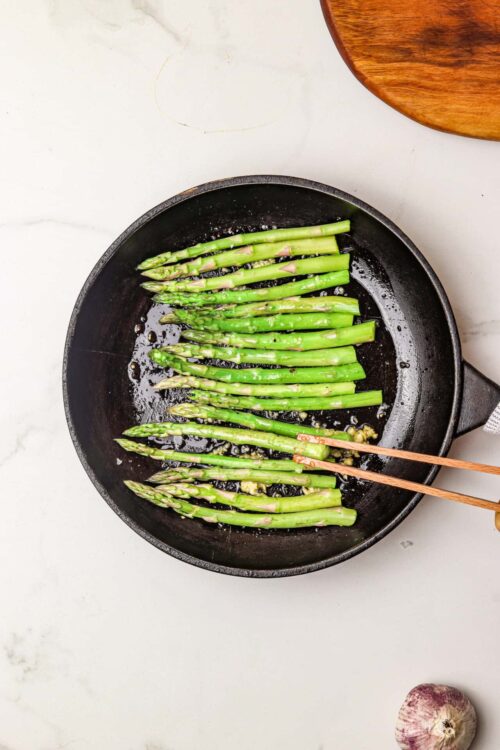 Freshly sautéed asparagus in a cast-iron skillet with garlic and olive oil. Perfect healthy side dish or ingredient for recipes.