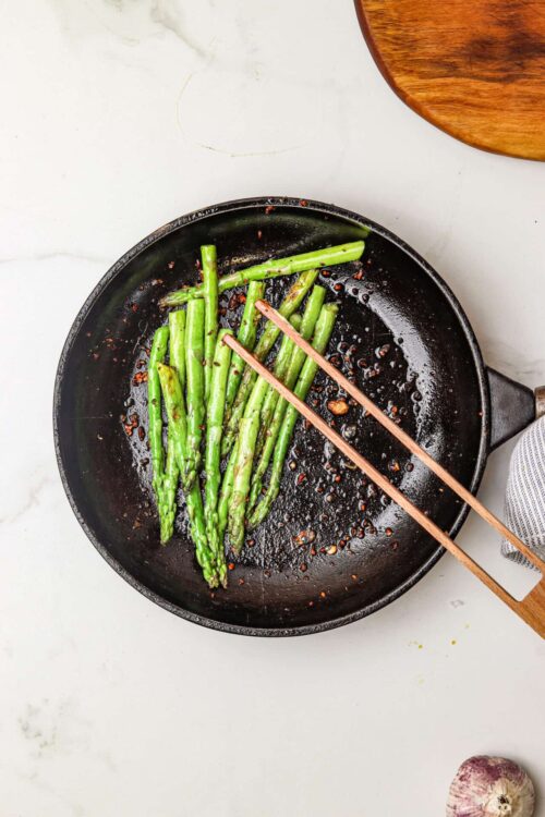 Sautéed asparagus spears in a cast iron skillet with garlic and red pepper flakes.