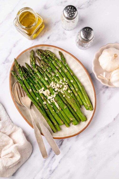 Roasted asparagus with garlic and olive oil on a ceramic platter.