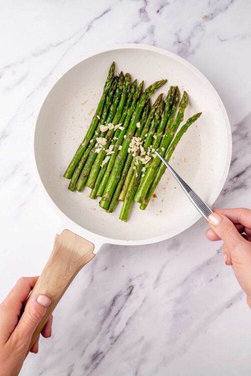 Freshly roasted asparagus with garlic and olive oil on a white skillet.